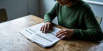 A person reviewing a detailed federal Pell Grant application form on a wooden table, emphasizing strategic planning for education funding. Their fingers are poised over the document, illuminated by cool ambient light.